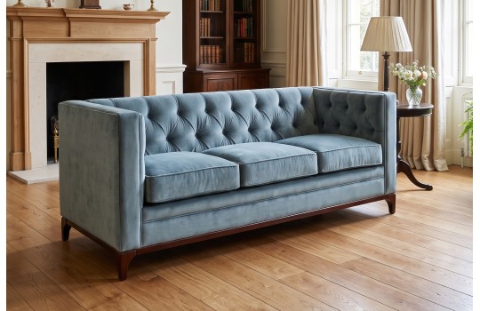 Sofa chesterfield z drewnianą podstawą Mobius 200 cm w niebieskim welurze w salonie z kominkiem
