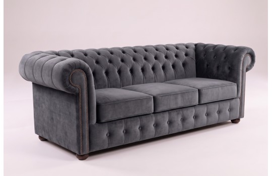 Trzyosobowa sofa chesterfield Noble w szarym welurze, ujęcie z boku Trzyosobowa sofa chesterfield Noble w szarym welurze, ujęcie z boku