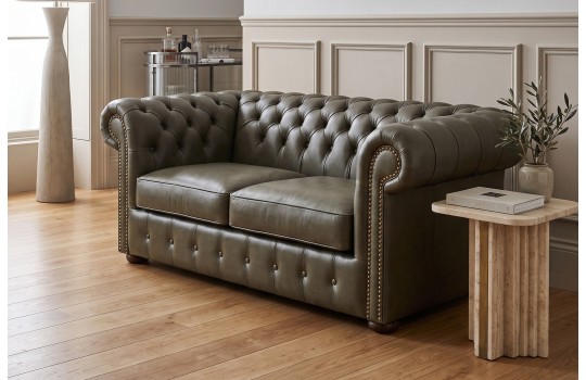 Kanapa chesterfield Noble w oliwkowoszarej skórze obok kamiennego stolika Kanapa chesterfield Noble w oliwkowoszarej skórze obok kamiennego stolika