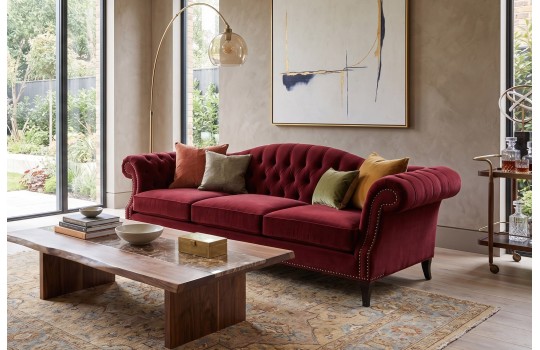 Bordowa kanapa wypoczynkowa w stylu chesterfield przy niskim stoliku w salonie Bordowa kanapa wypoczynkowa w stylu chesterfield przy niskim stoliku w salonie
