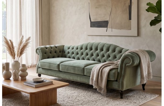 Szałwiowa sofa welurowa chesterfield Solano z jasnym pledem przy drewnianym stoliku