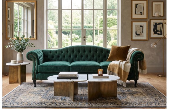 Butelkowozielona sofa chesterfield Solano w eleganckim salonie z dużym oknem i dywanem