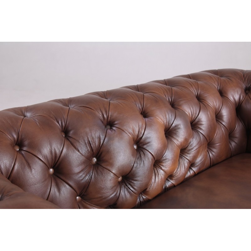 Pikowanie guzikami w skórze naturalnej – zbliżenie na brązowe lico narożnika chesterfield Pikowanie guzikami w skórze naturalnej – zbliżenie na brązowe lico narożnika chesterfield