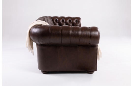 Ciemnobrązowa skórzana sofa chesterfield – ujęcie z boku, widoczny wałek i podłokietnik Ciemnobrązowa skórzana sofa chesterfield – ujęcie z boku, widoczny wałek i podłokietnik