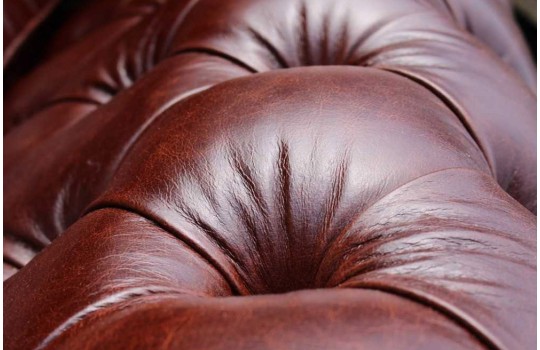 Pikowanie guzikami w skórze – zbliżenie na bordowe lico kanapy chesterfield Foster Pikowanie guzikami w skórze – zbliżenie na bordowe lico kanapy chesterfield Foster