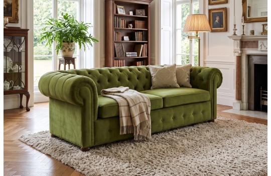 Sofa chesterfield Mati w oliwkowej zieleni w salonie z kominkiem i regałem Sofa chesterfield Mati w oliwkowej zieleni w salonie z kominkiem i regałem